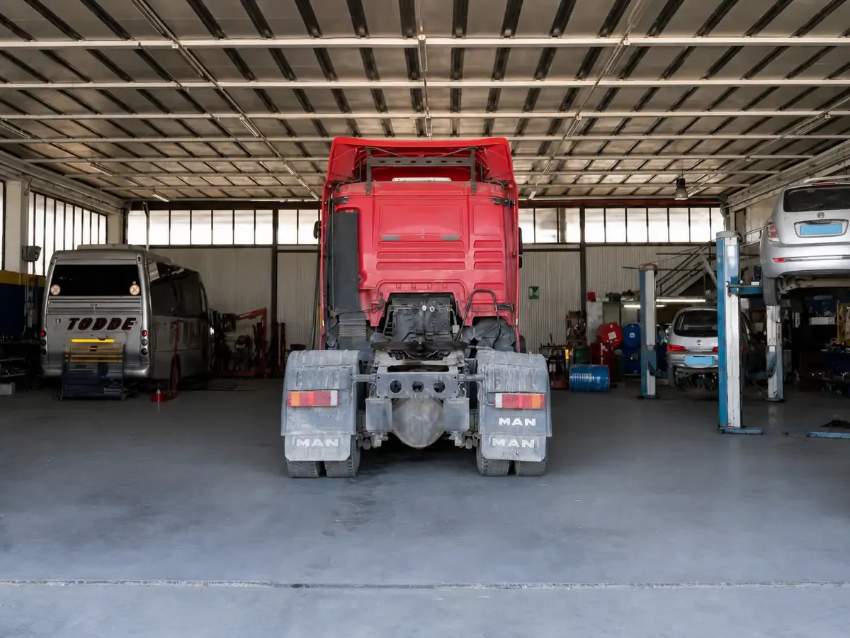 Trattore stradale MAN rosso fermo in officina, davanti ai ponti sollevatori